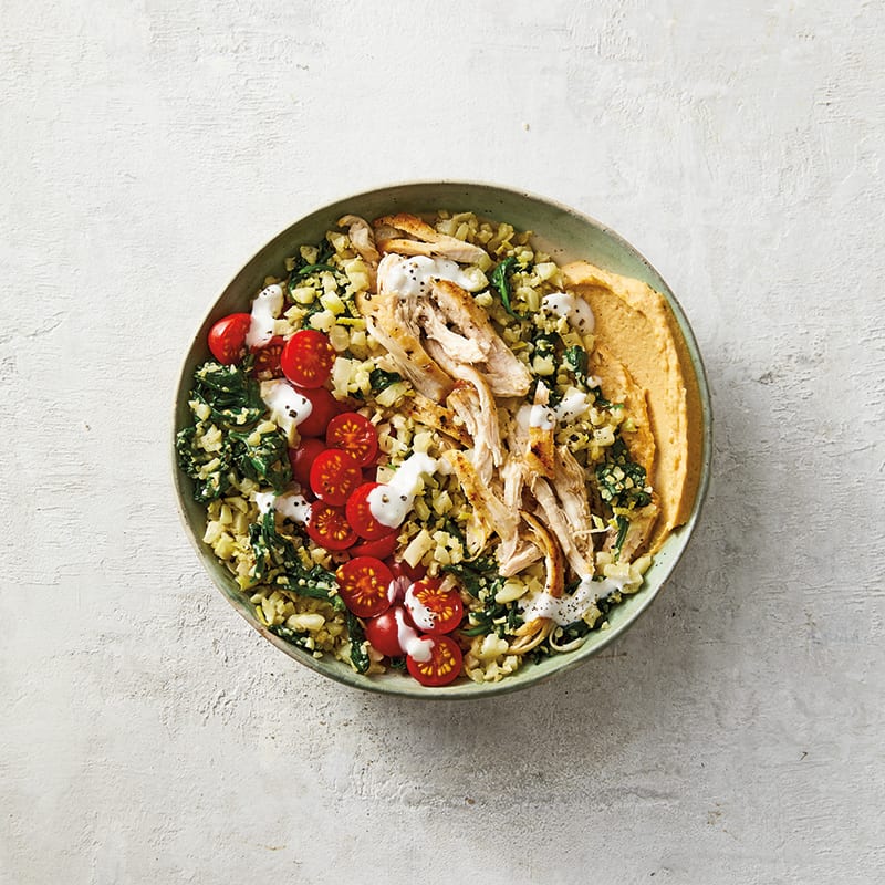 individual serving bowl with spinach-cauliflower rice topped with chicken, tomatoes, hummus, and a creamy feta sauce