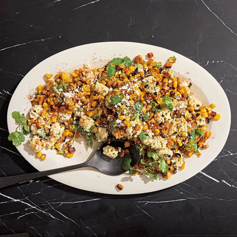A large oval white serving plate topped with a Mexican corn and pasta salad garnished with cotija cheese and cilantro.