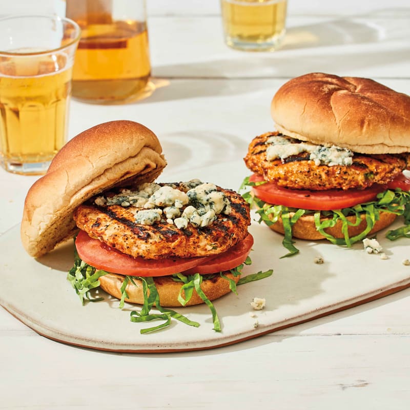 two chicken burgers on rolls topped with blue cheese, lettuce and tomatoes