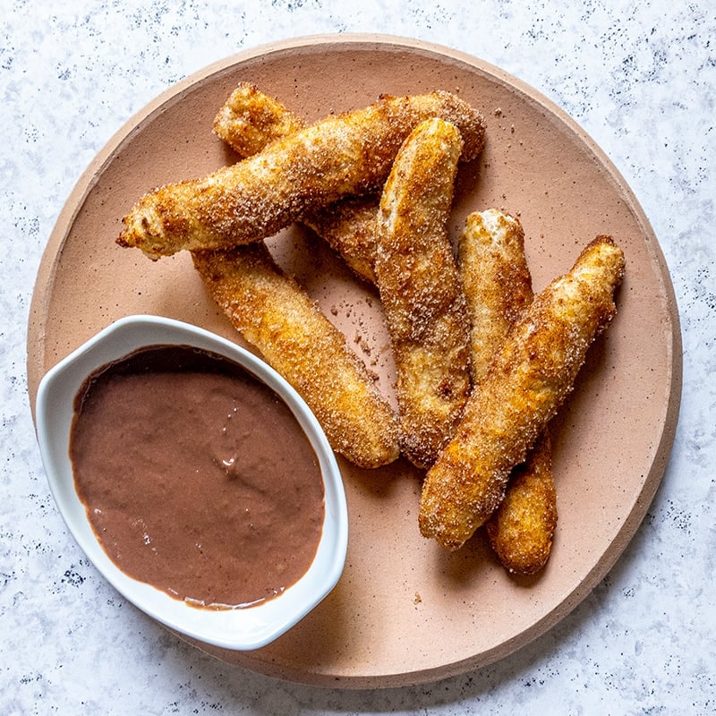 Air fried churros on a light brown plate with a small white bowl of chocolate dipping sauce on the side