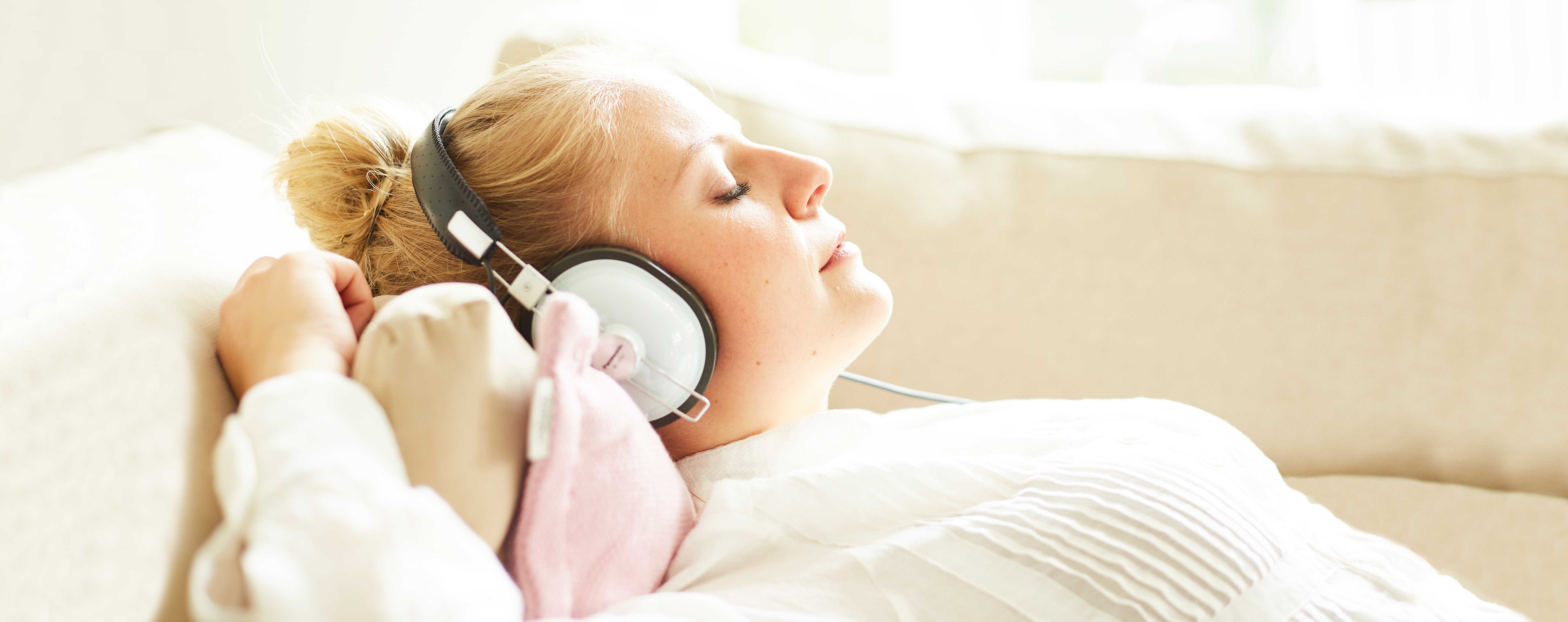 Une jeune femme écoute de la musique sur le canapé, les yeux fermés