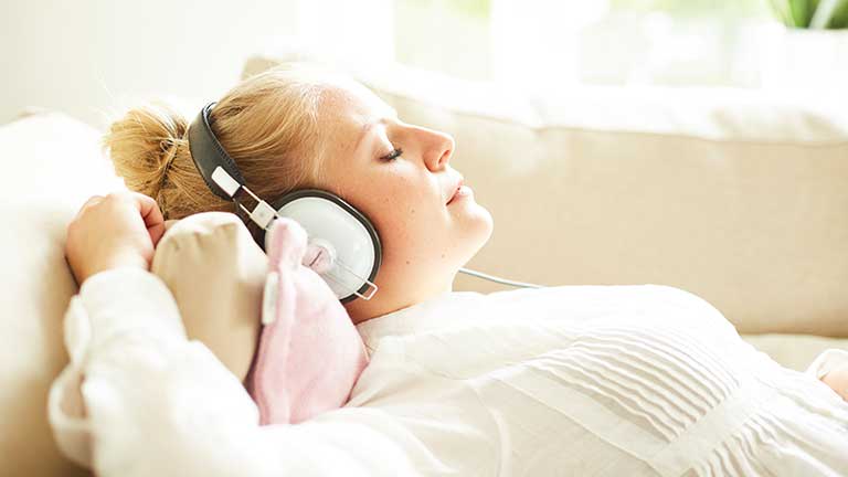 Junge Frau hört mit geschlossenen Augen auf dem Sofa Musik