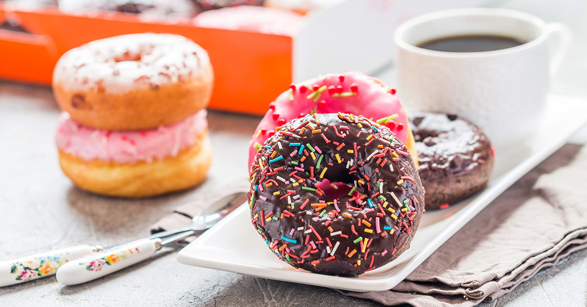 Strawberry cream–filled donut, chocolate frosted donut with sprinkles, and cup of coffee