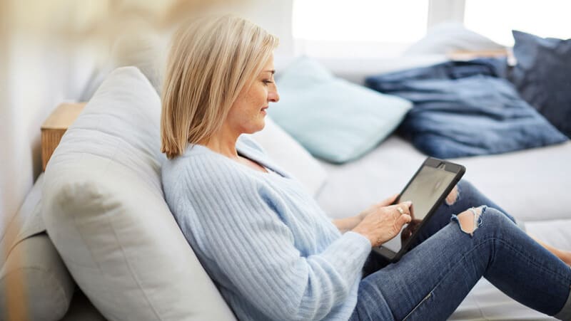 Frau mit blonden Haaren in hellblauem Pullover schaut auf Tablet 