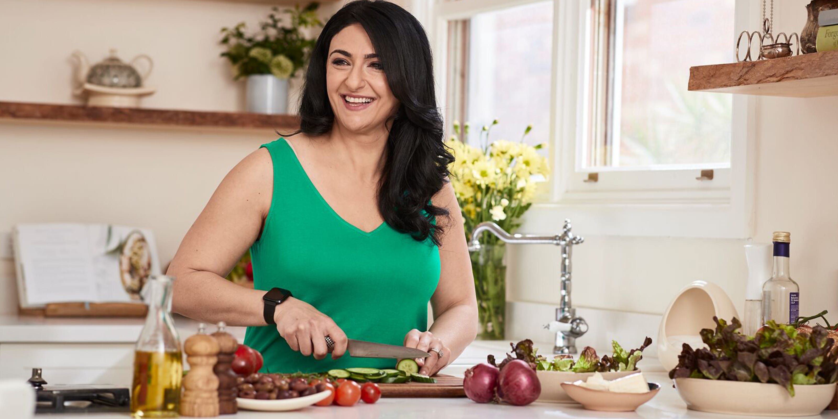 Frau mit dunklen Haaren und grünem Kleid schneidet Gemüse in der Küche