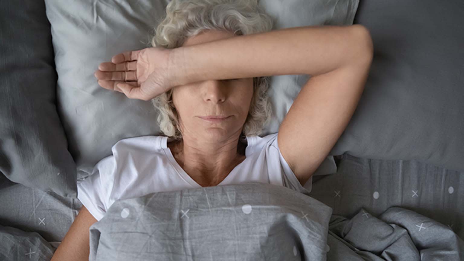 Frau liegt im Bett und verschränkt Arm über dem Gesicht 