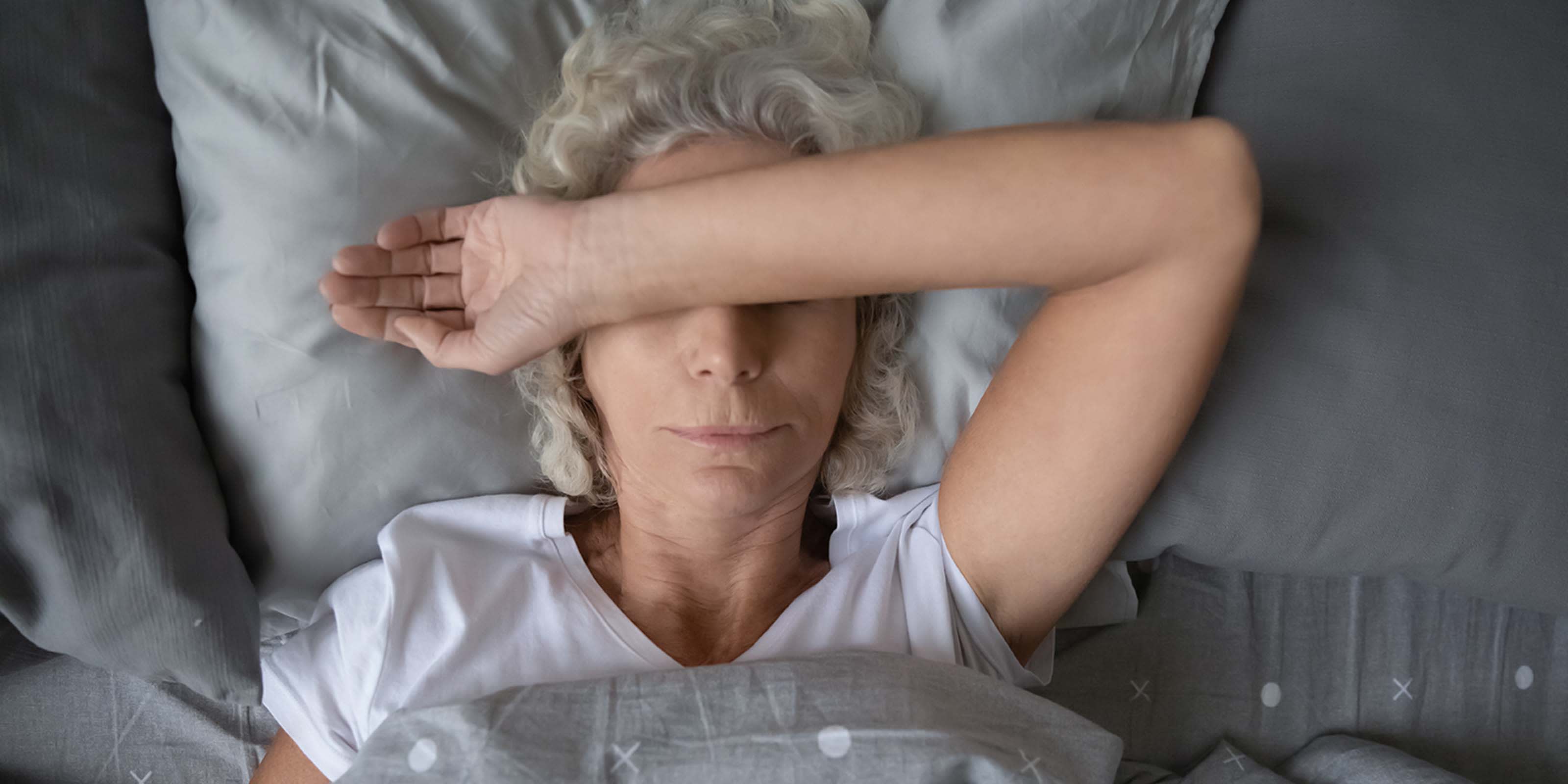 Une femme couchée dans le lit, les bras croisés sur le visage 