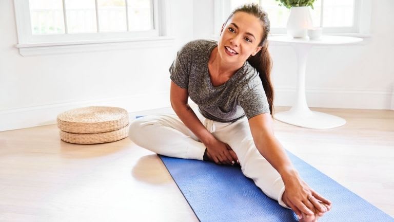 Junge Frau in Sportkleidung dehnt sich auf Yogamatte.