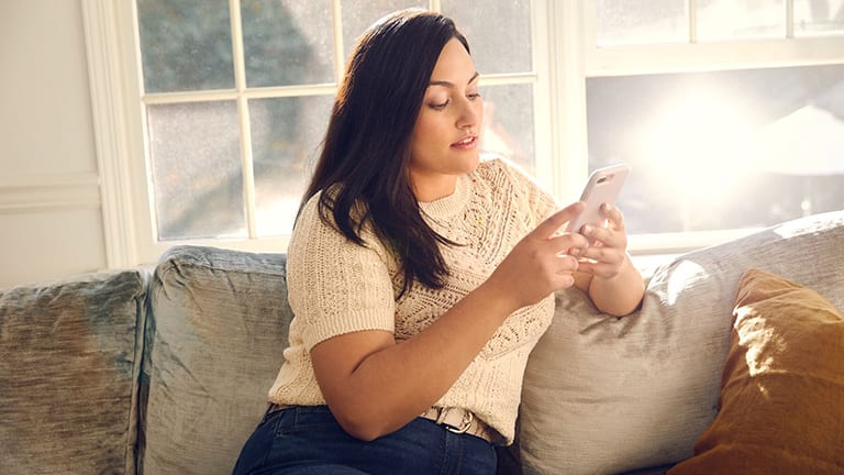 Femme assise sur un canapé et regardant son téléphone portable