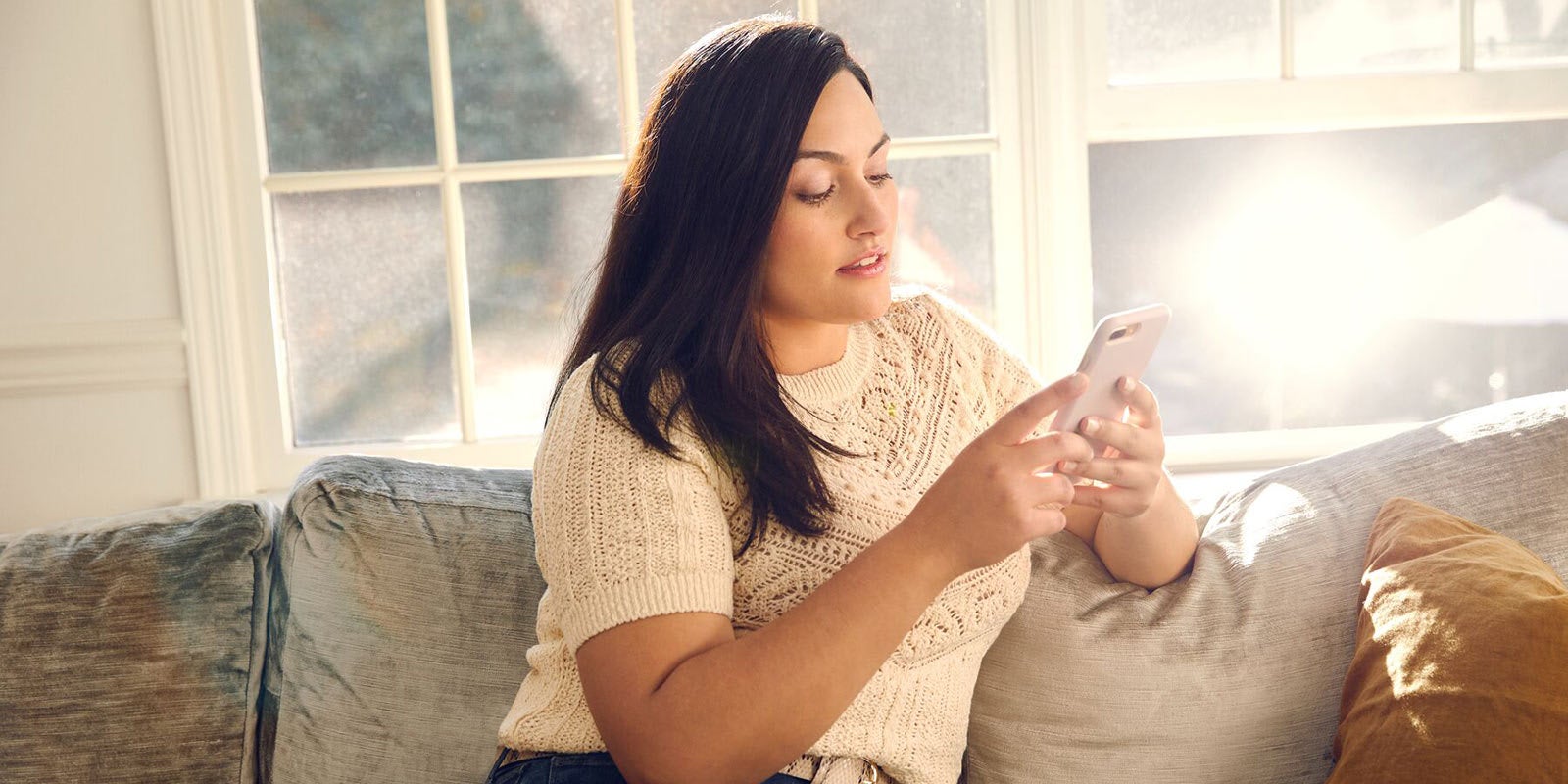 Femme assise sur un canapé et regardant son téléphone portable