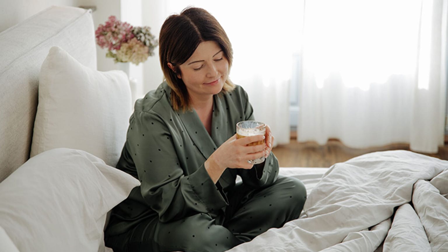 WW Mitglied Dominika sitzt in grünem Pyjama mit einer Tasse Kaffee im Bett