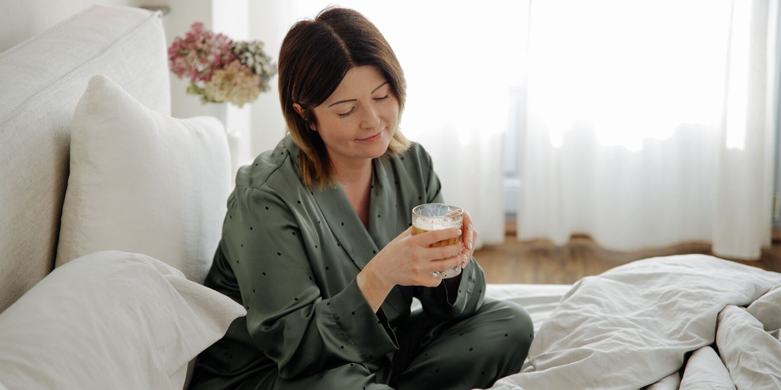 WW Mitglied Dominika sitzt in grünem Pyjama mit einer Tasse Kaffee im Bett