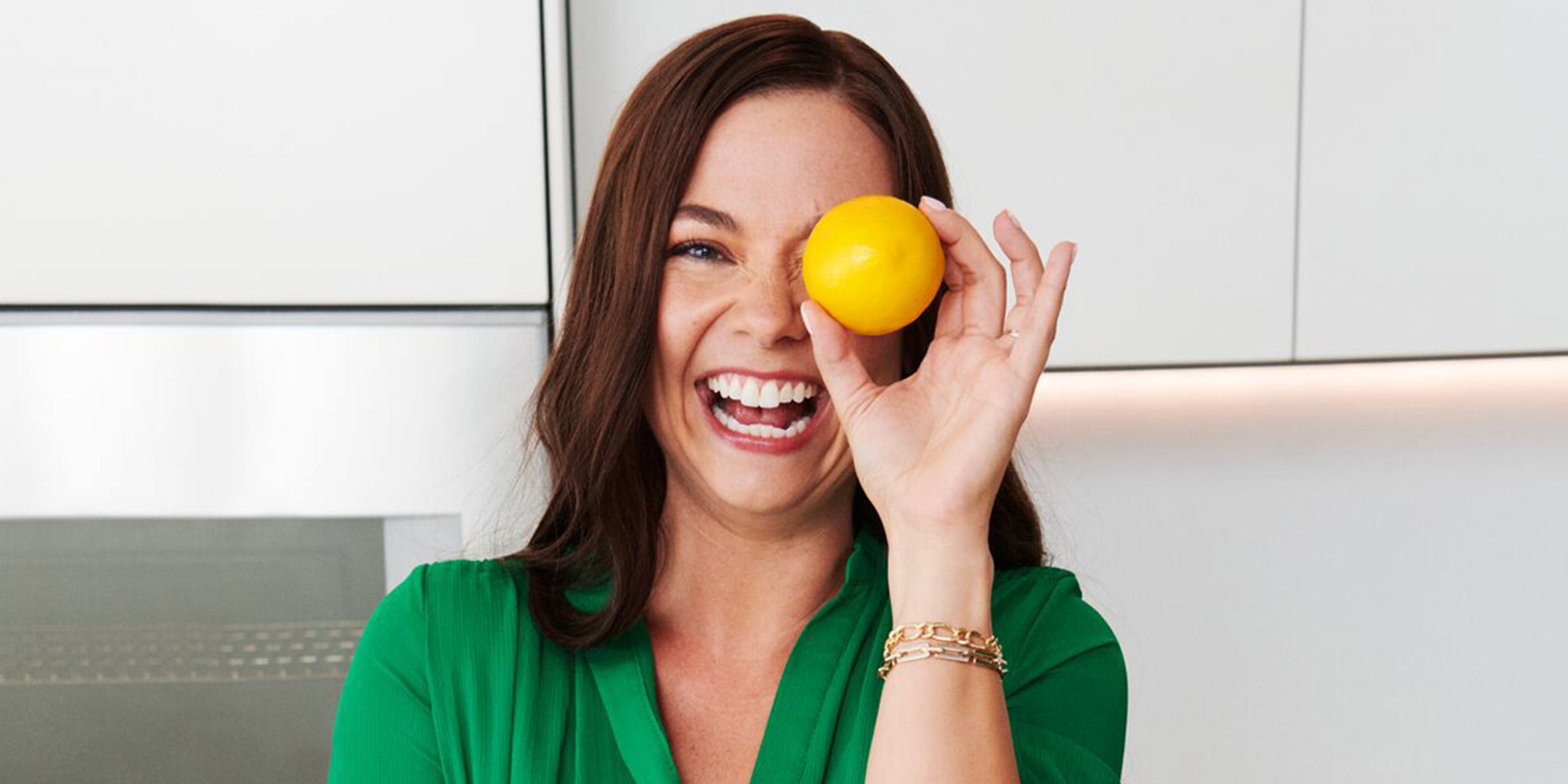 Une femme rit en tenant un citron devant son visage