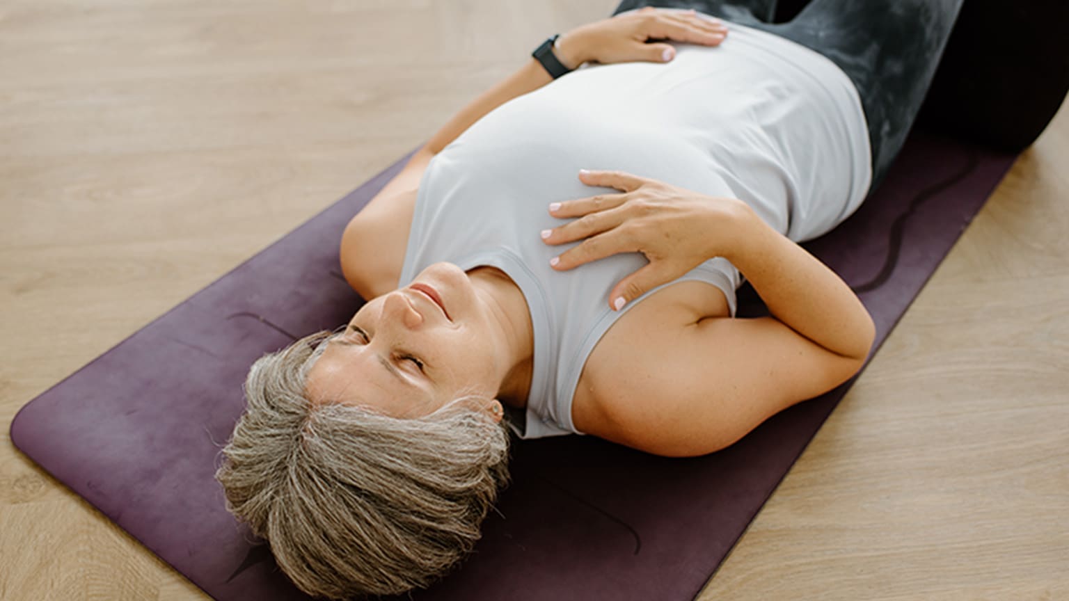 Eine Frau liegt mit geschlossenen Augen auf einer Yoga-Matte.