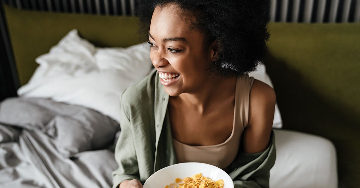 Woman sitting up in bed with a bowl of cereal