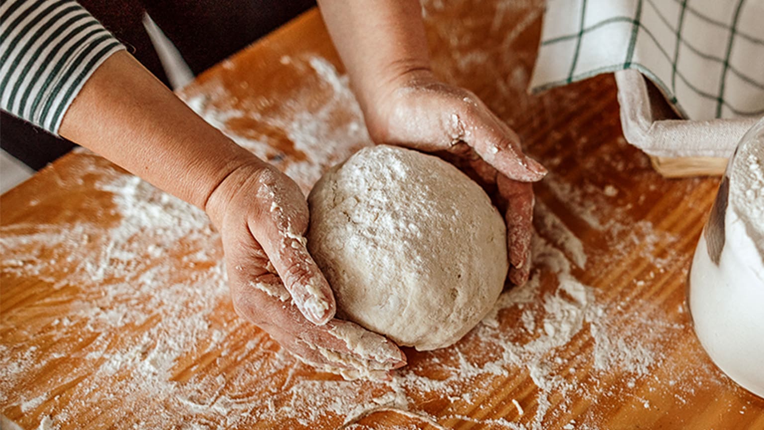 Une femme forme une boule de pâte sur une surface farinée.