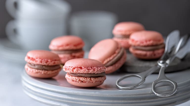 Auf einem Teller liegen rosa Macarons gefüllt mit einer Schokocreme