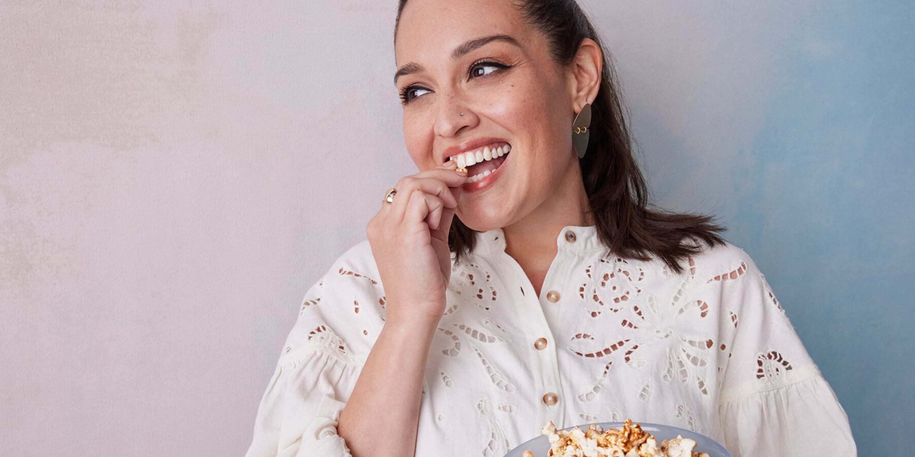 Junge Frau mit braunen Haaren in weißer Bluse isst Popcorn