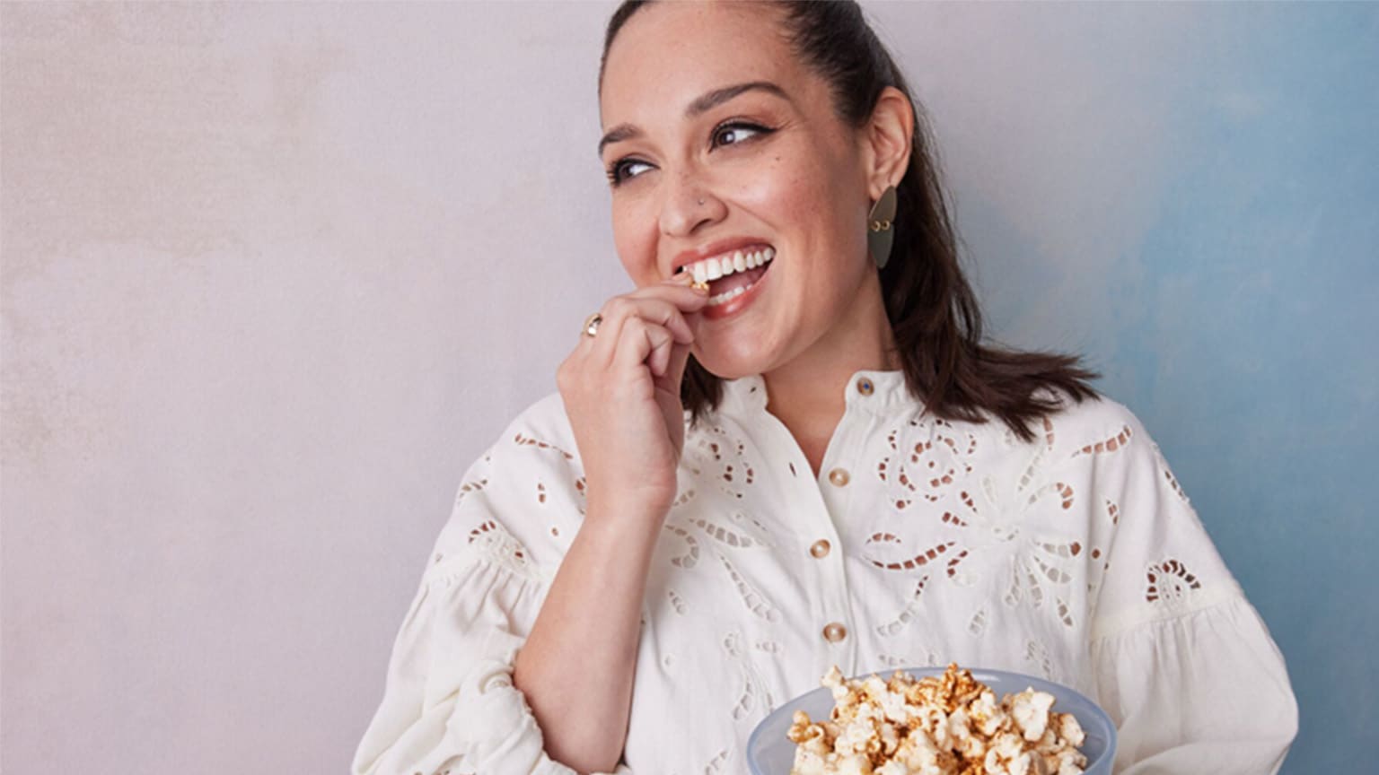 Junge Frau mit braunen Haaren in weißer Bluse isst Popcorn