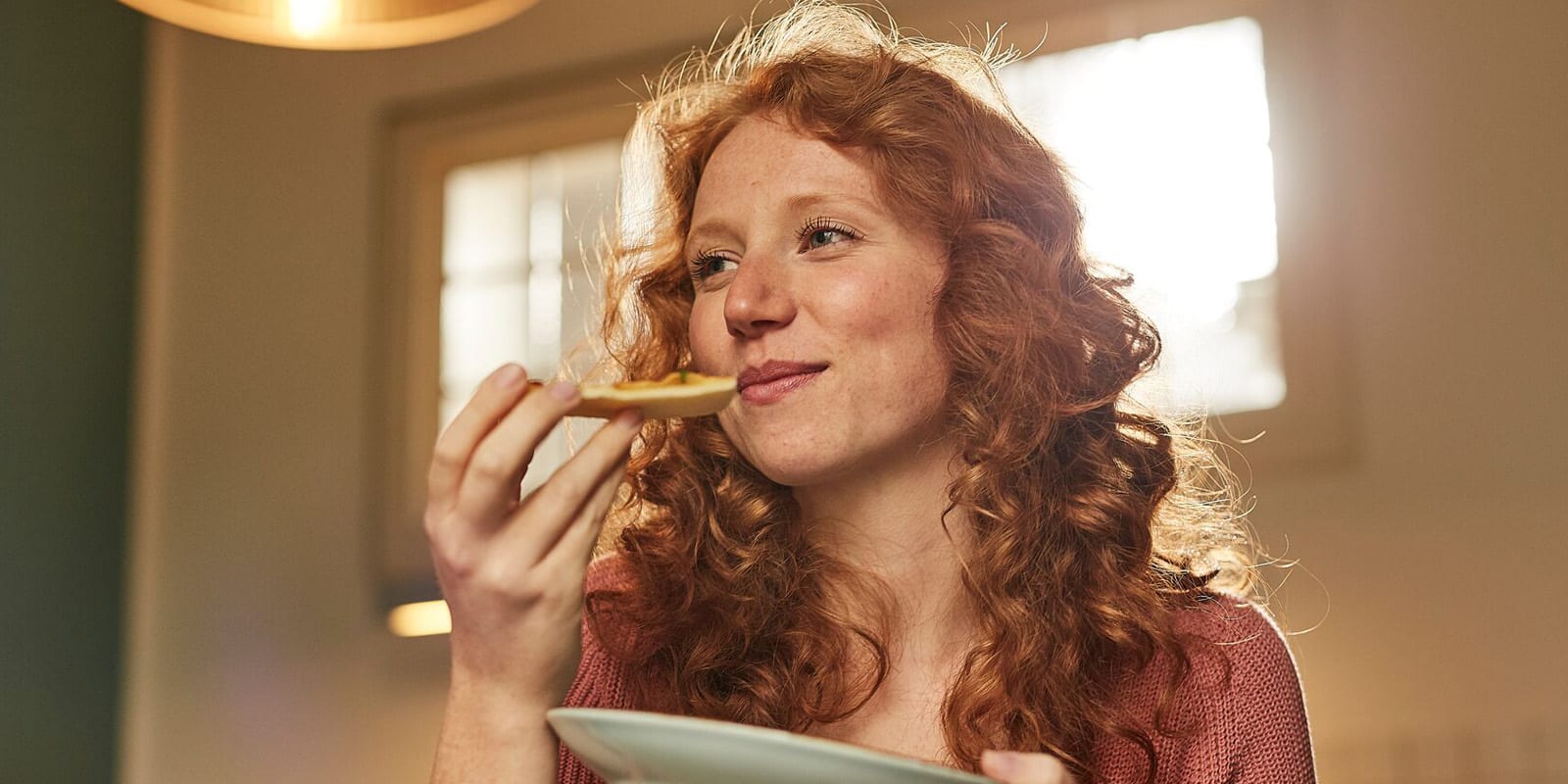 Junge Frau mit roten Haaren isst ein Stück Pizza.