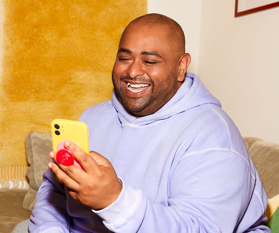 Man seated on couch holding an iphone and smiling at the phone screen.