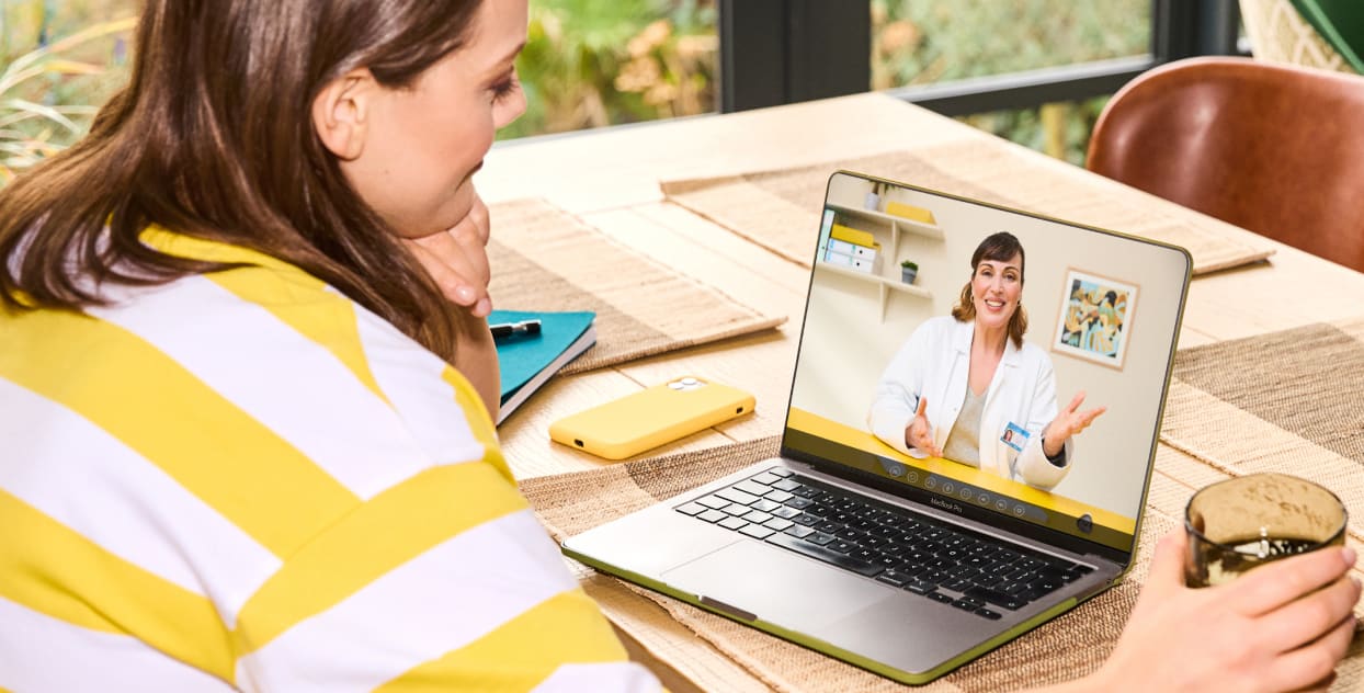 Woman having telehealth consultation with clinician on a laptop from her kitchen.