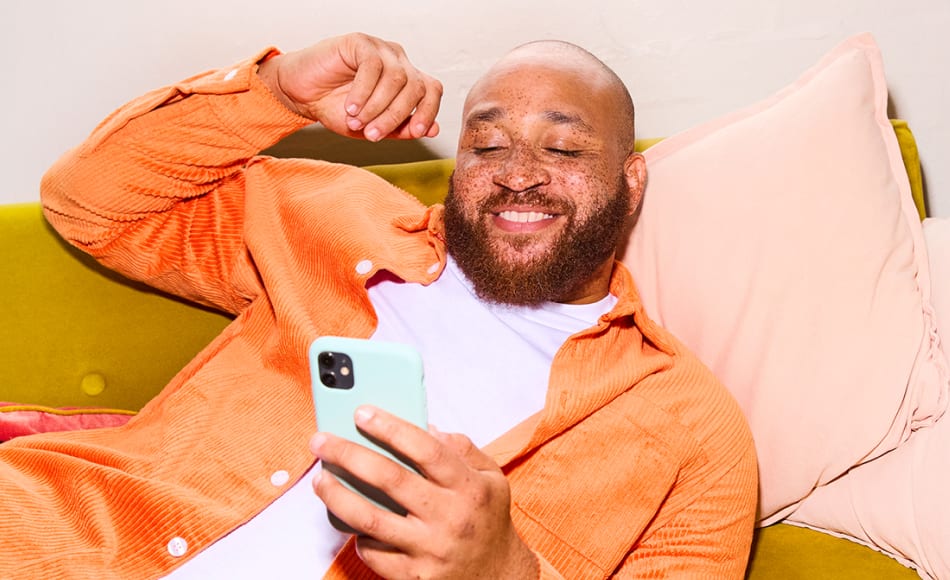 Man relaxing on sofa, holding and looking at his iphone and smiling.