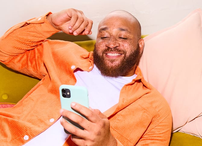 Man relaxing on sofa, holding and looking at his iphone and smiling.