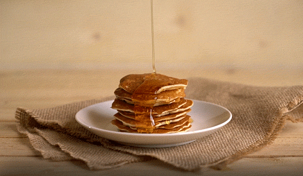 Maple syrup being poured on a stack of pancakes