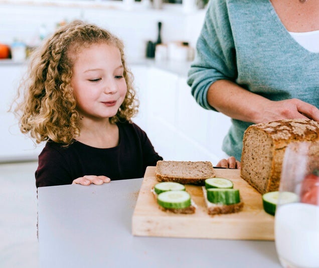 Kind schaut ihrer Mutter beim Brotschmieren zu.