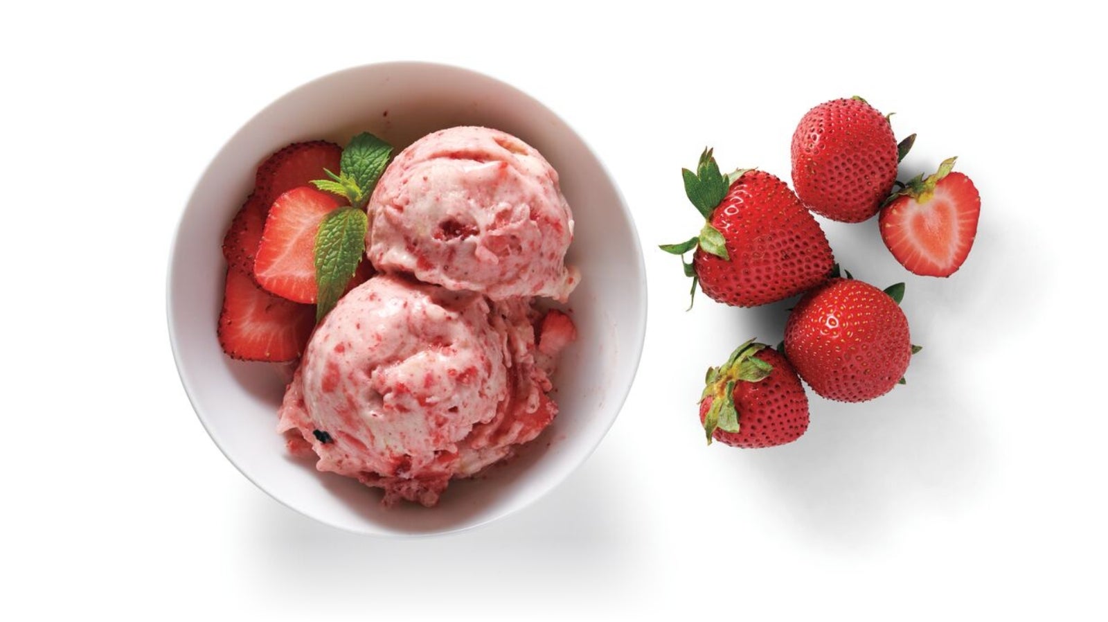 A bowl of strawberry ice cream with 5 strawberries sitting next to it