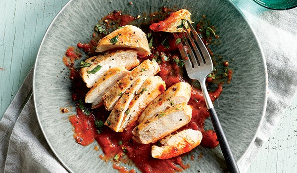 Photo shows sliced cooked chicken breast plated with red-pepper sauce