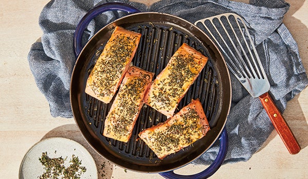 Photo shows four herb-crusted salmon fillets cooking in a grill pan