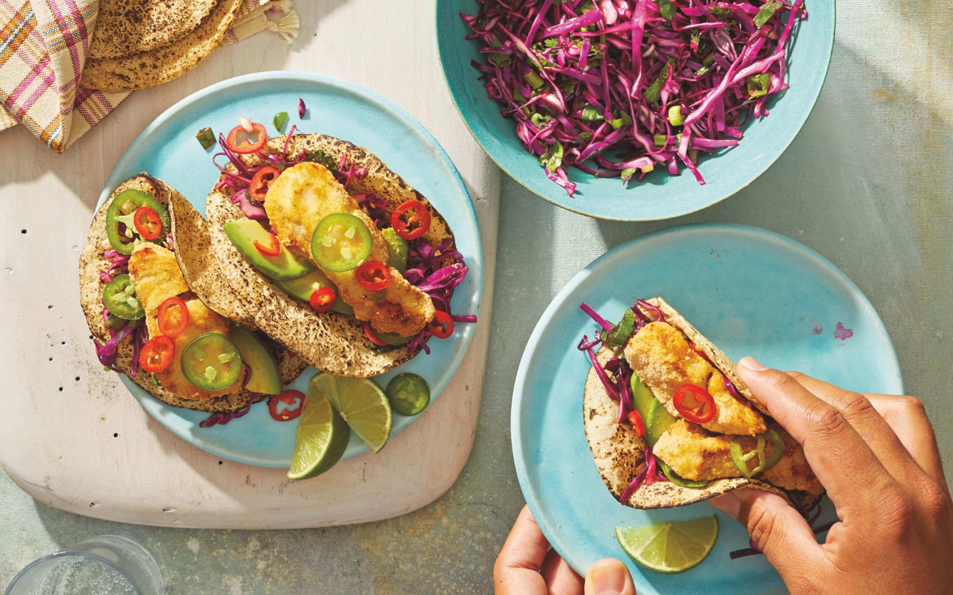 Fish tacos on plates alongside fresh tortillas.