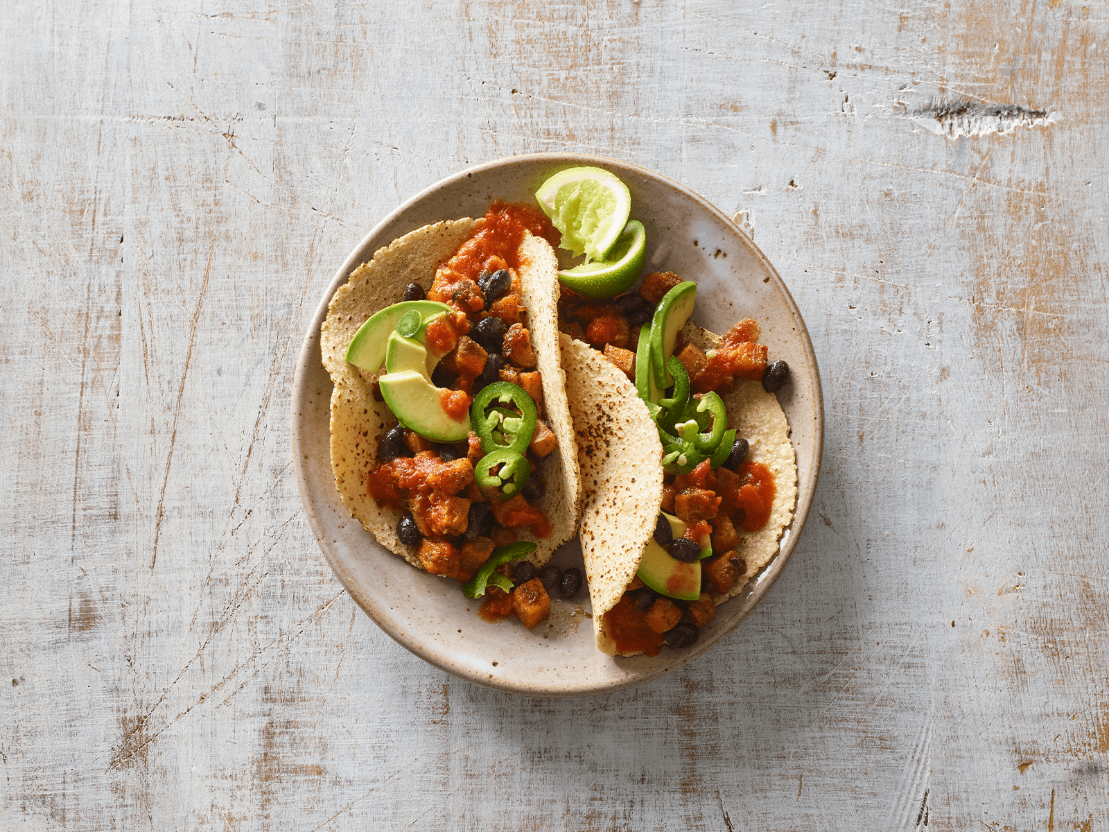 Mit Avocado und Hänhnchen gefüllte Tacos auf beigem Teller