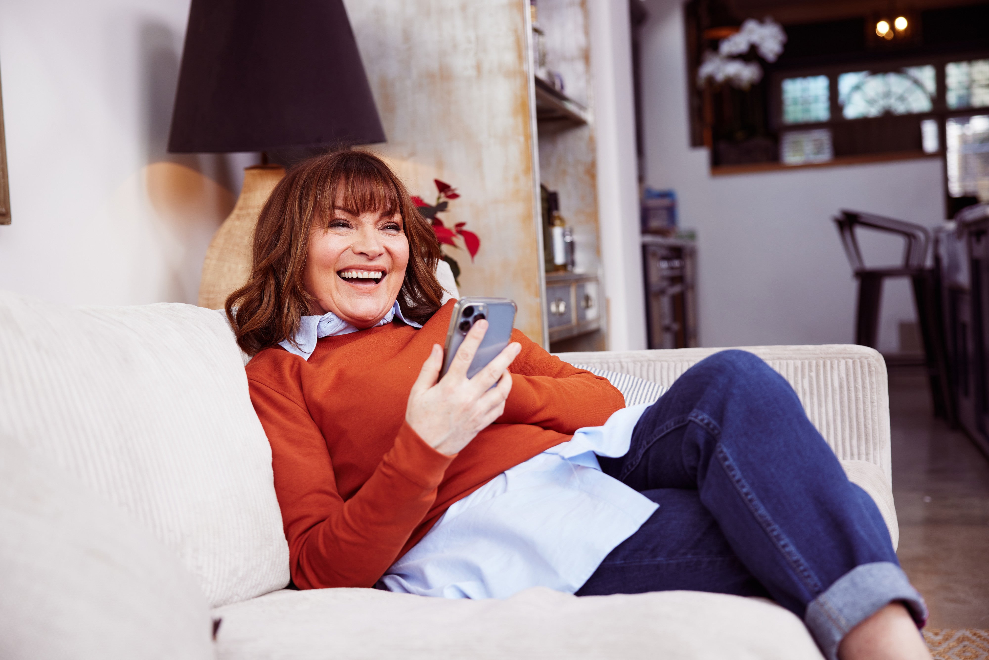 Image of Lorraine Kelly smiling on her sofa holding a phone