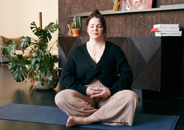 Paula Lambert sitzt meditierend im Schneidersitz auf Matte